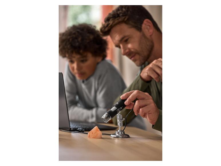 Vater und Sohn untersuchen einen rosa Stein mit einem Digitalmikroskop.