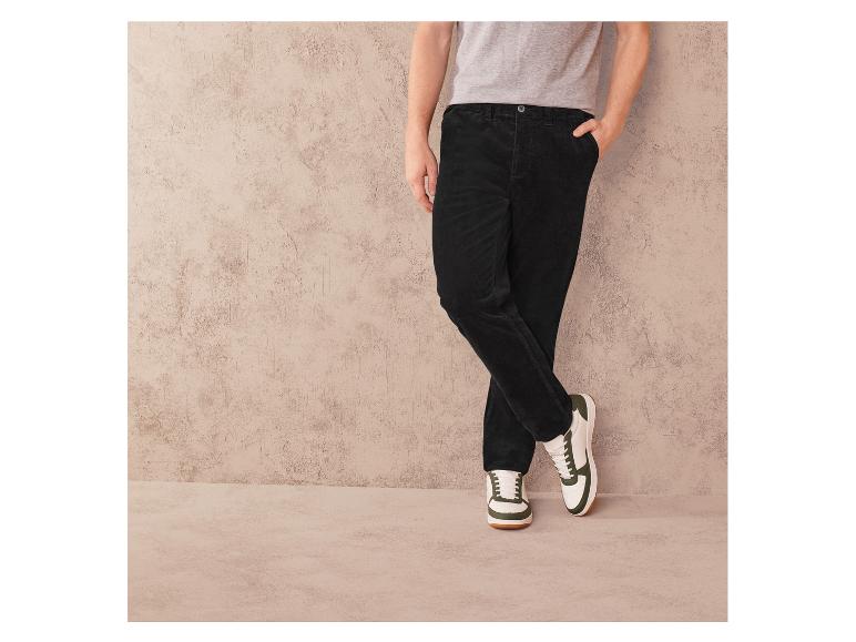 Schwarze Cordhose und weiße Sneaker mit grünen Akzenten.