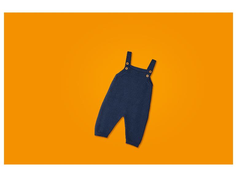 Dunkelblauer gestrickter Baby-Strampler mit Trägern und Holzknöpfen, auf orangefarbenem Hintergrund.