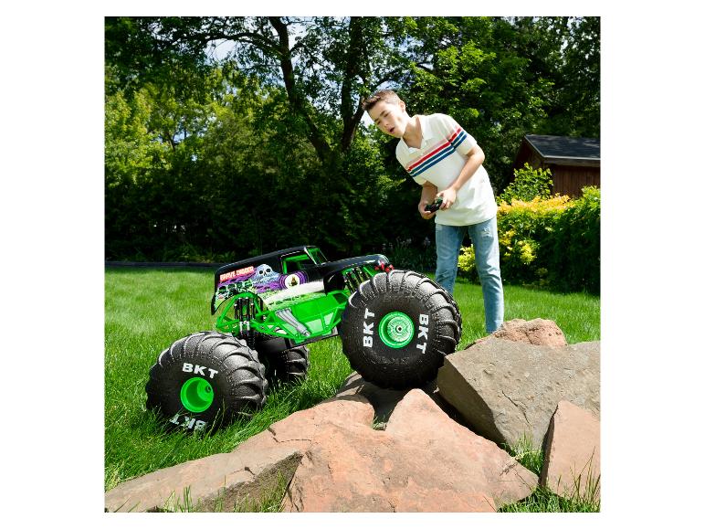 Ein Junge steuert einen Grave Digger RC Monstertruck auf Gras, mit Felsen im Vordergrund.