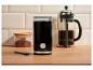 Schwarze elektrische Kaffeemühle, French Press und gemahlener Kaffee in einem Glas auf Holzarbeitsplatte.
