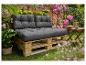 Outdoor-Palettensofa mit dunkelgrauen Kissen, umgeben von üppigem Grün und rosa Blüten.