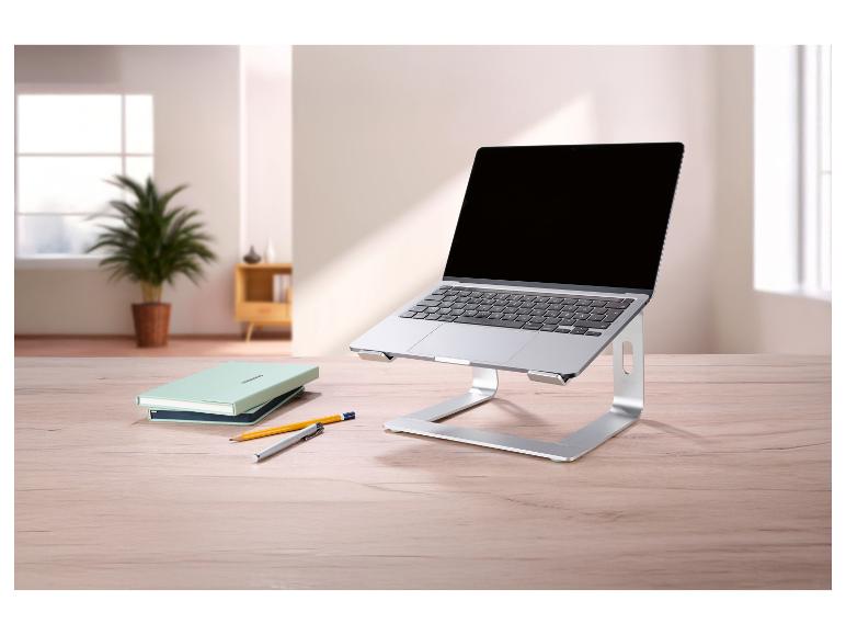 Silberner Laptopständer mit Laptop, Notizbüchern und Stiften auf einem Holztisch.