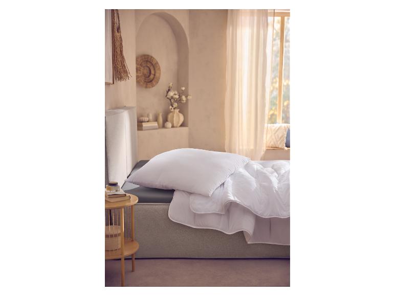 Weiße Bettdecke und Kissen auf einem Bett in einem hellen Schlafzimmer mit Fenster.