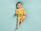 Ein Baby in einem gelben Winnie-Puuh-Body auf blauem Untergrund.