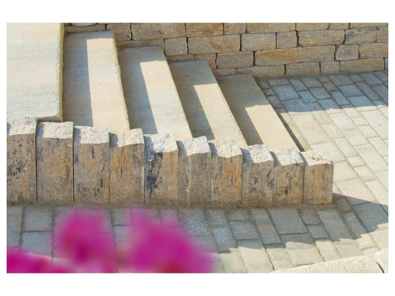 Außensteintreppe mit Stützmauer und Pflastersteinen, mit unscharfen rosa Blumen im Vordergrund.