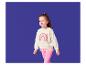 Mädchen in cremefarbenem Sweatshirt mit Regenbogen-Print und pinken Leggings.
