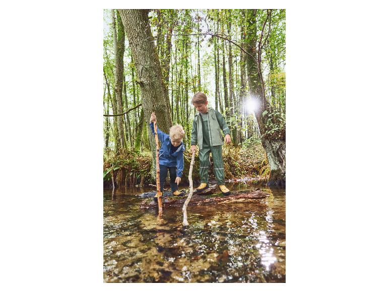 Zwei Jungen in wasserdichten Jacken und Hosen spielen in einem Bach im Wald.