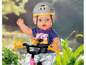 Baby-Puppe mit Helm auf einem Fahrrad.