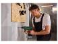 Mann bohrt mit einem Akku-Bohrhammer in eine Wand, Werkzeuge an einer Holzplatte im Hintergrund.