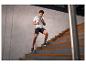 Mann in Sportkleidung rennt Treppe hoch, trägt graues T-Shirt und schwarze Shorts.