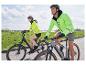 Zwei Personen fahren Fahrrad und tragen leuchtend gelbe Sicherheitsjacken.