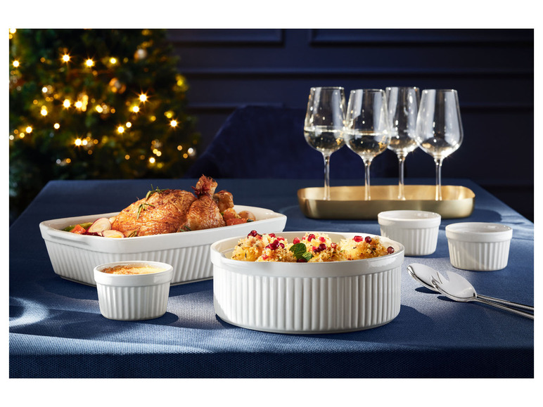Weiße Auflaufform mit gebratenem Hähnchen, kleine Auflaufform mit Dessert und Weingläser.