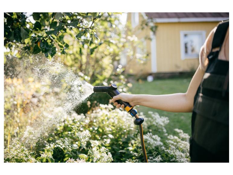 Person bewässert Pflanzen im Garten mit einer Gießpistole.