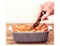Lasagne in einer grauen Auflaufform wird mit einem Messer geschnitten.