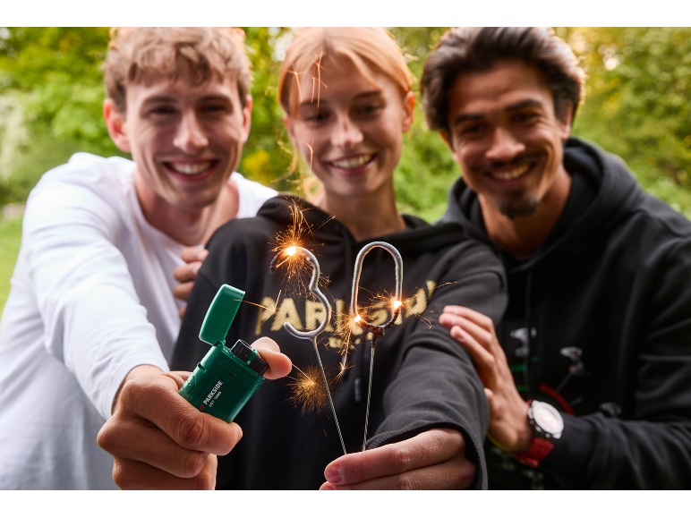 Drei lächelnde Personen halten Wunderkerzen und ein grünes Feuerzeug.