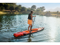 Mann paddelt auf einem Stand-Up-Paddle-Board auf einem See, umgeben von Bäumen und Bergen.