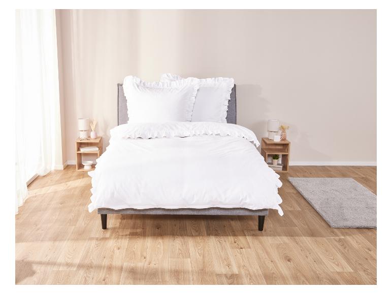 Weiße Bettwäsche mit Rüschen auf einem Bett in einem Schlafzimmer.