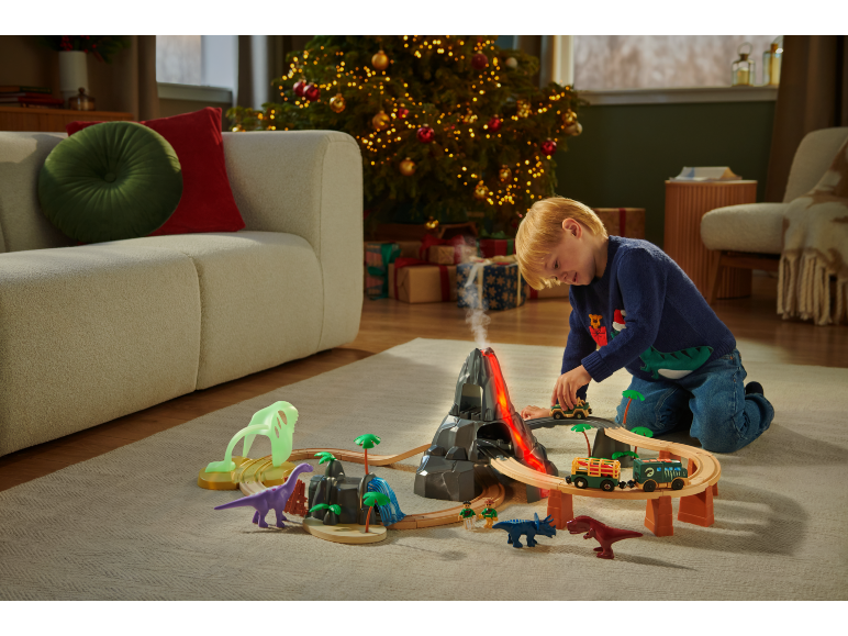 Kind spielt mit Zug und Dinosauriern in einem weihnachtlichen Wohnzimmer.