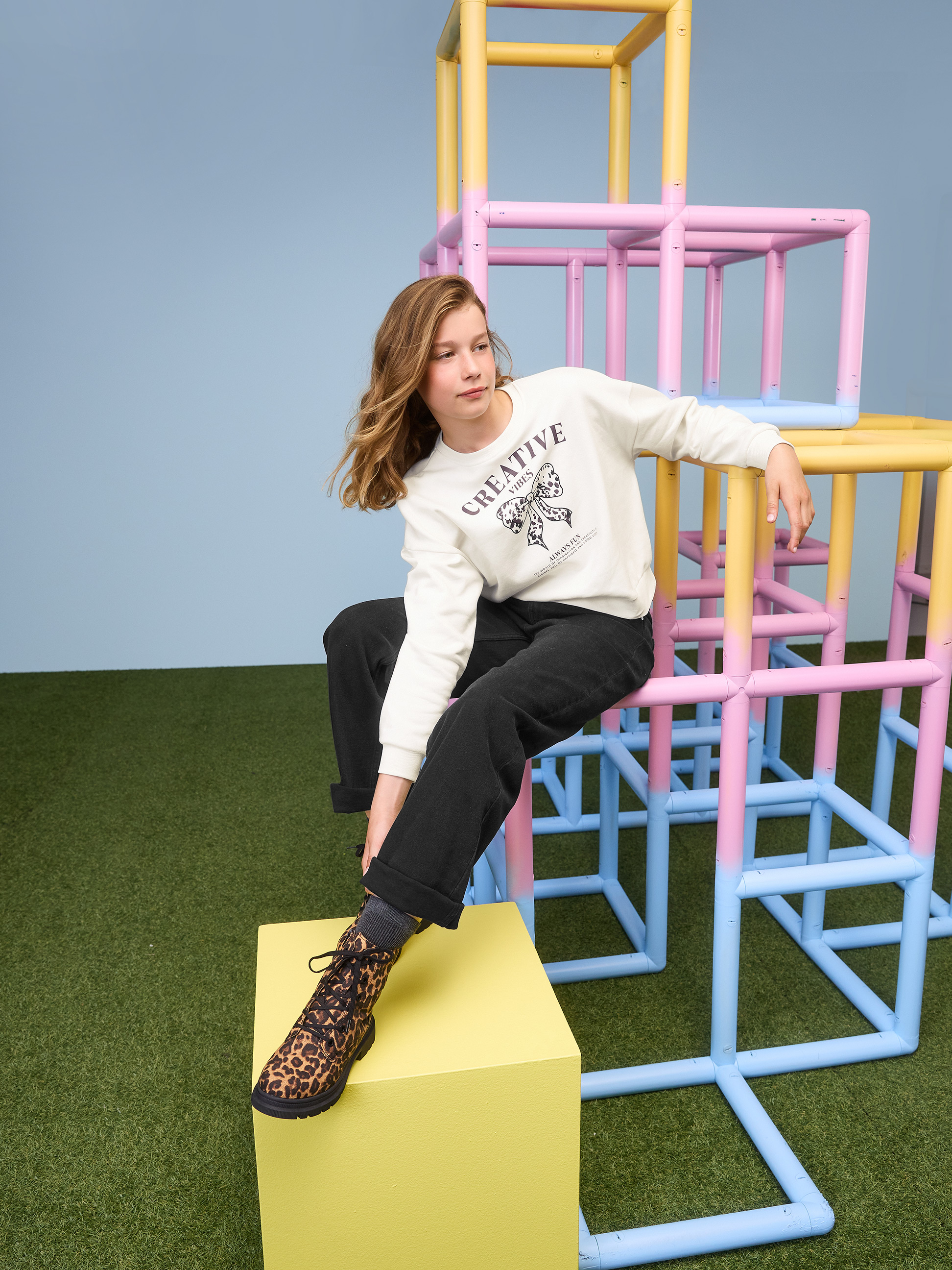 Mädchen in weißem Creative Vibes Sweatshirt und schwarzer Hose auf einem Klettergerüst.