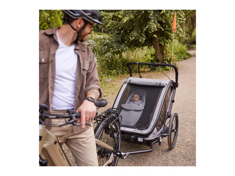 Mann mit Fahrrad und Hauck Fahrradanhänger mit Baby