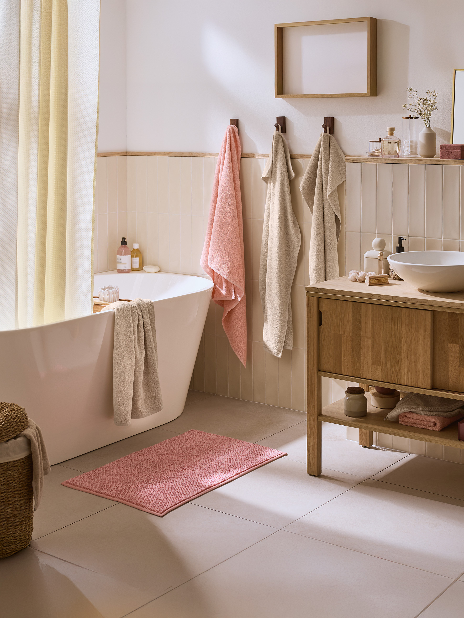 Helles Badezimmer mit Badewanne, Holzwaschtisch und rosa und beigen Handtüchern.