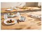 Elegantes weißes Geschirr mit Fleisch- und Linsengericht, Salat und Kaffee auf einem Holztisch.