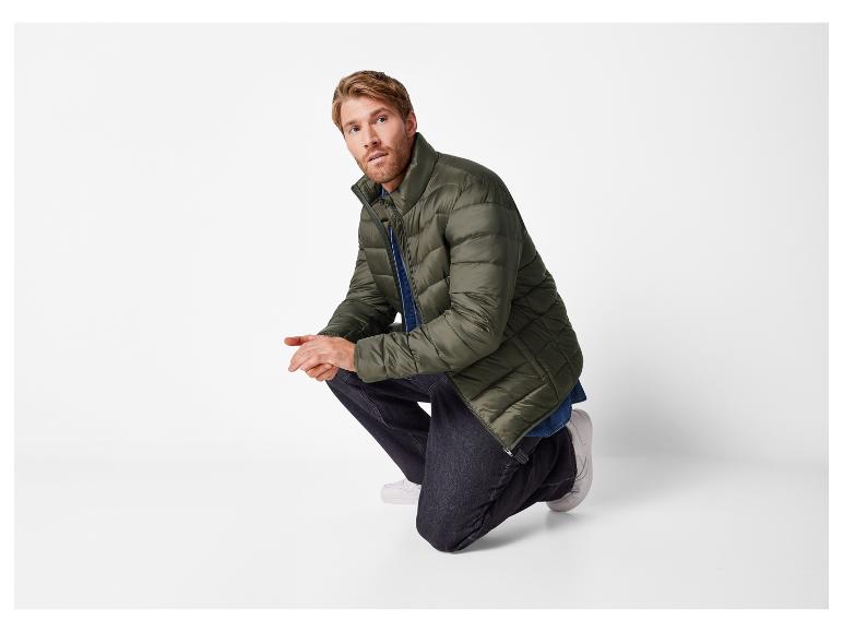 Ein Mann kniet in einer grünen Daunenjacke und dunklen Jeans.