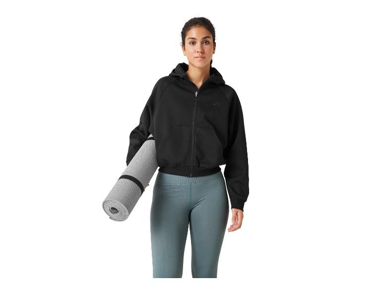 Frau mit Kapuzenjacke und Leggings trägt eine Yogamatte.