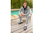 Mann in grauem Trainingsanzug und schwarzen Sandalen mit weißen Socken, lächelt und hält einen grünen Smoothie.