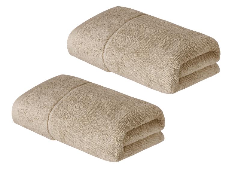 Zwei Stapel hellbeige Handtücher vor weißem Hintergrund.