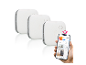 Drei weiße Rauchmelder mit einer Smart-Home-App auf einem Smartphone.