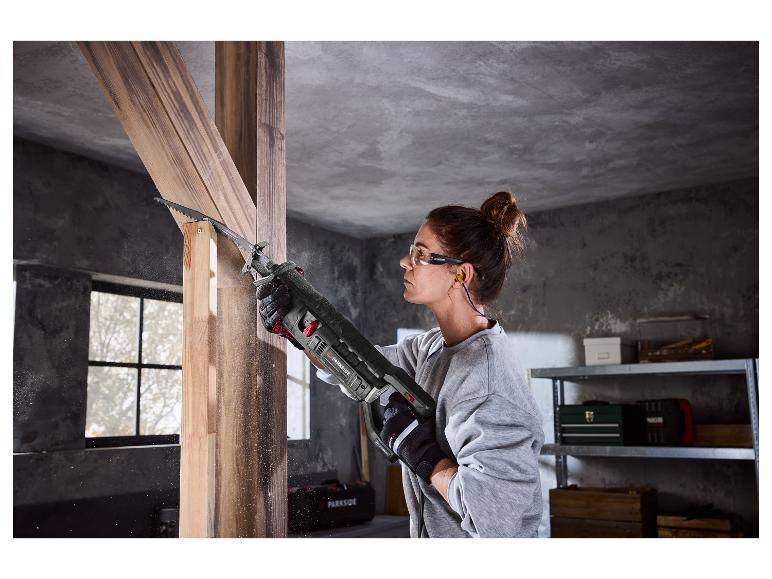Frau sägt Holz mit einer Säbelsäge, trägt Schutzbrille und Gehörschutz.