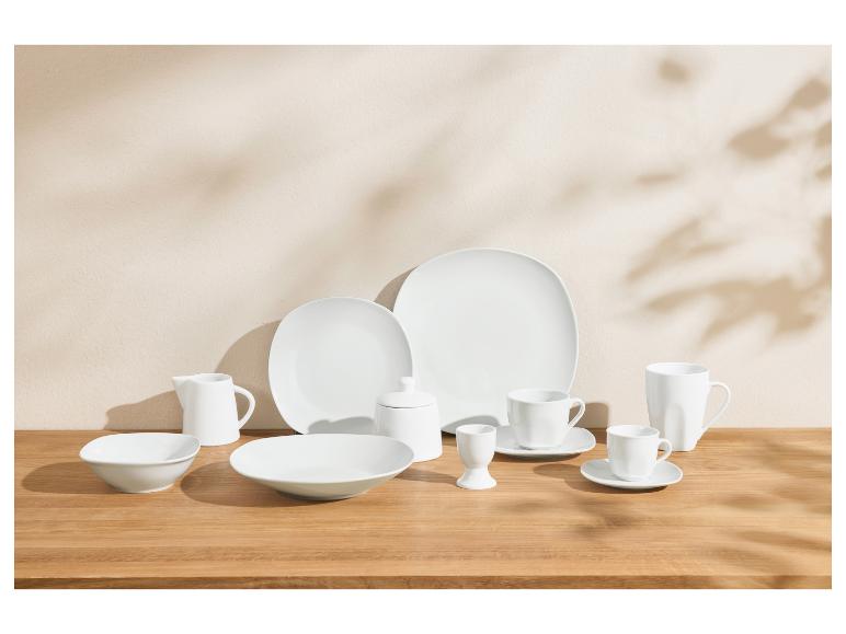 Weißes Porzellangeschirr-Set mit Tellern, Schalen, Tassen und Servierteilen auf einem Holztisch.
