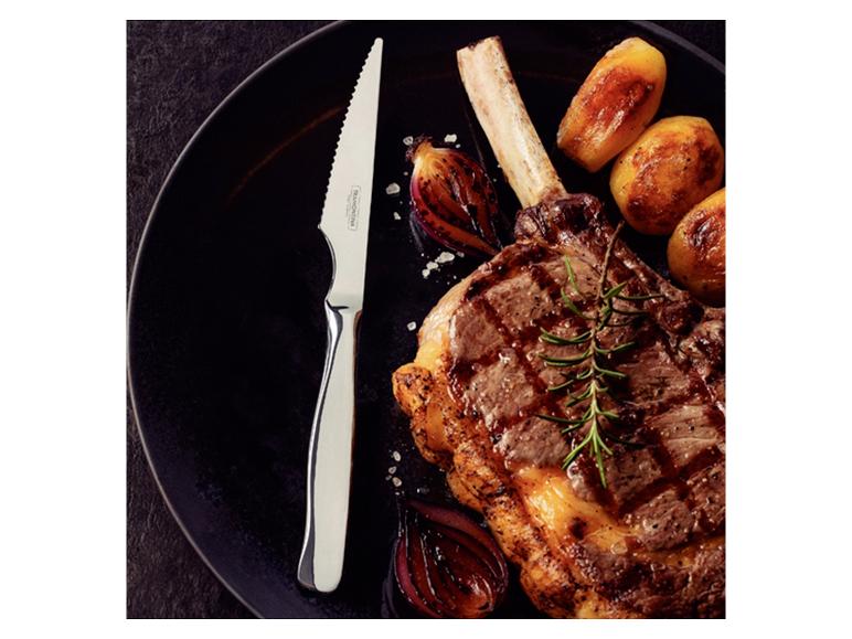 Knochensteak mit Bratkartoffeln, Zwiebeln und Rosmarin auf einem schwarzen Teller, mit Messer.