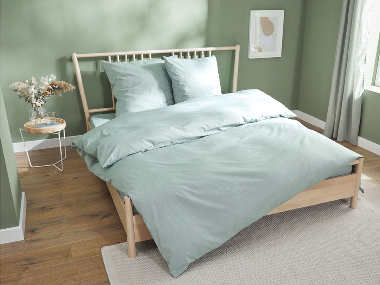 Ein Bett mit hellgrünem Bettbezug und Kissen in einem ruhigen Schlafzimmer.