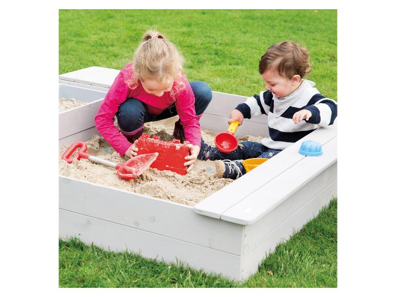 Kinder spielen in einem Holzsandkasten mit Sandspielzeug.