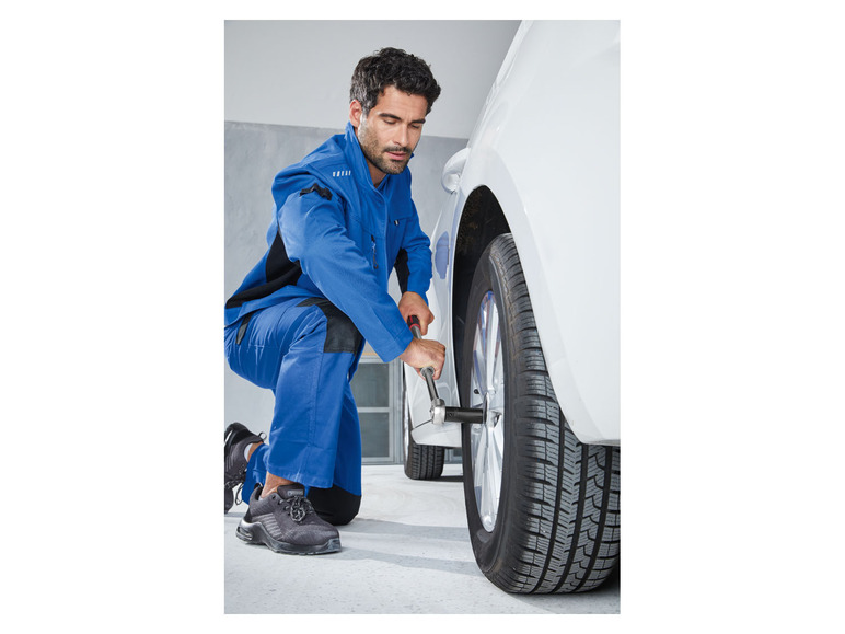 Ein Mechaniker in Arbeitskleidung wechselt ein Reifen an einem Auto.