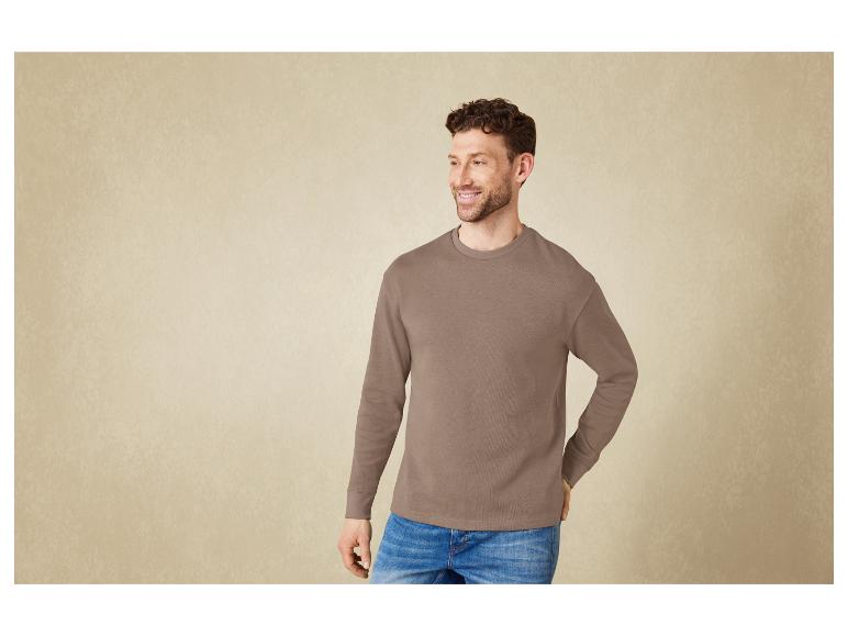 Mann in einem dunkelbraunen Sweatshirt und blauen Jeans.