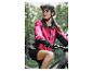 Eine Frau in einer pinken Fahrradjacke und einem schwarzen Helm auf einem E-Bike im Wald.