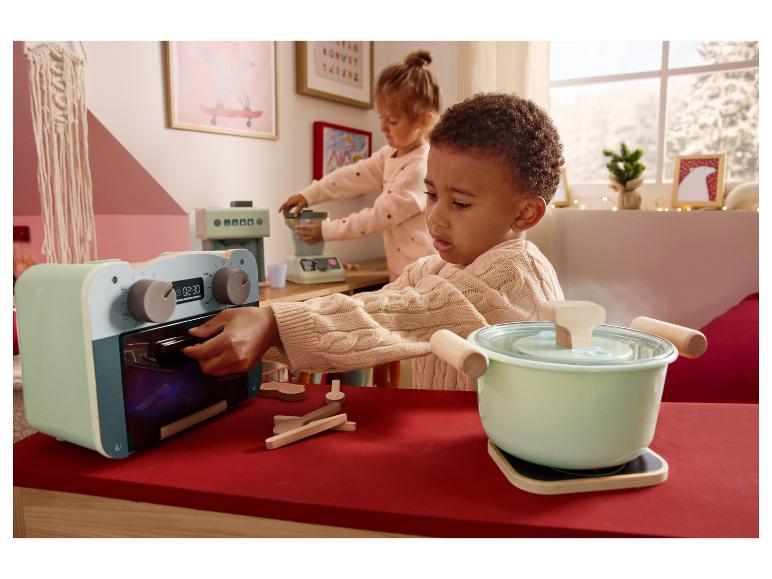 Zwei Kinder spielen mit Spielzeugküchengeräten, darunter einem Ofen und einem Topf.