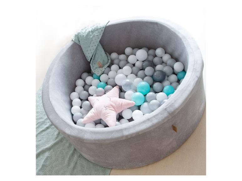 Ein grauer Ballpool mit weißen, grauen und türkisfarbenen Bällen und einem rosafarbenen Sternkissen.