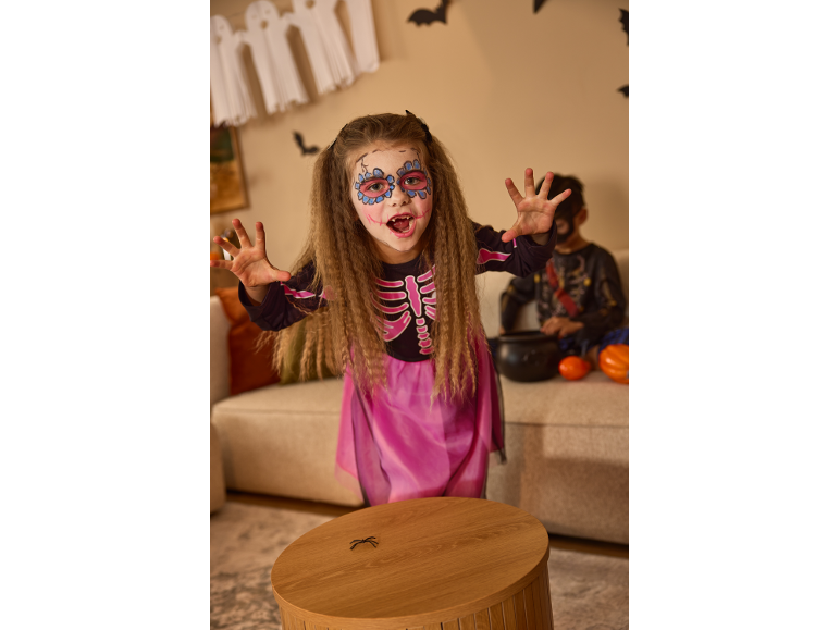 Mädchen im Skelettkostüm und Halloween-Gesichtsbemalung, mit ausgestreckten Händen zur Kamera.