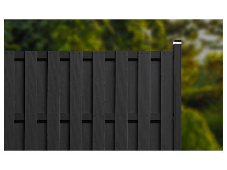 Schwarzer Zaun mit vertikalen Latten und beleuchtetem Pfosten vor verschwommenem Grün.