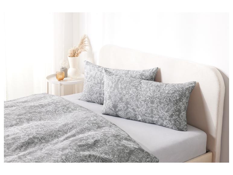 Ein Bett mit einem grauen Bettbezug mit einem weißen Paisley-Muster und passenden Kissen.