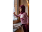 Kleinkind im rosa Pullover mit Bär und weinroter Schlupfmütze schaut aus dem Fenster im Schnee.