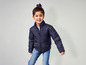 Ein Mädchen trägt eine blaue Winterjacke und Jeans.