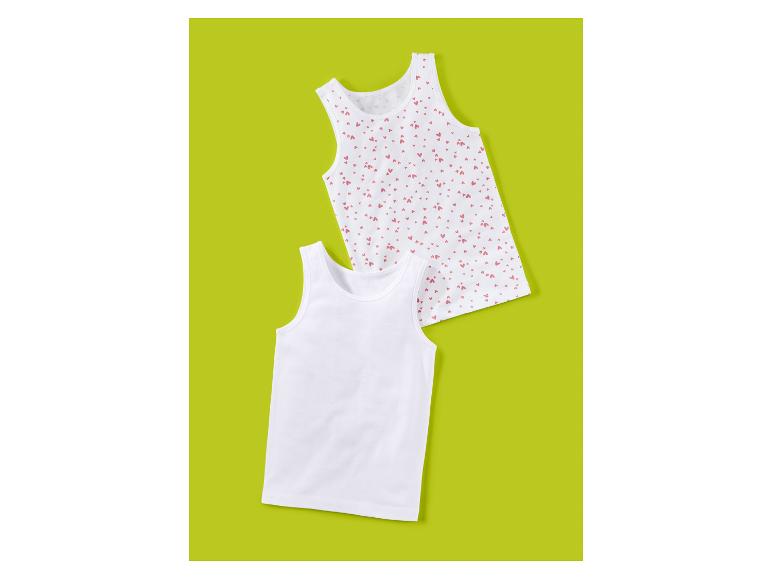 Zwei weiße Kinder-Unterhemden, eines schlicht und eines mit rosa Herzchenmuster.