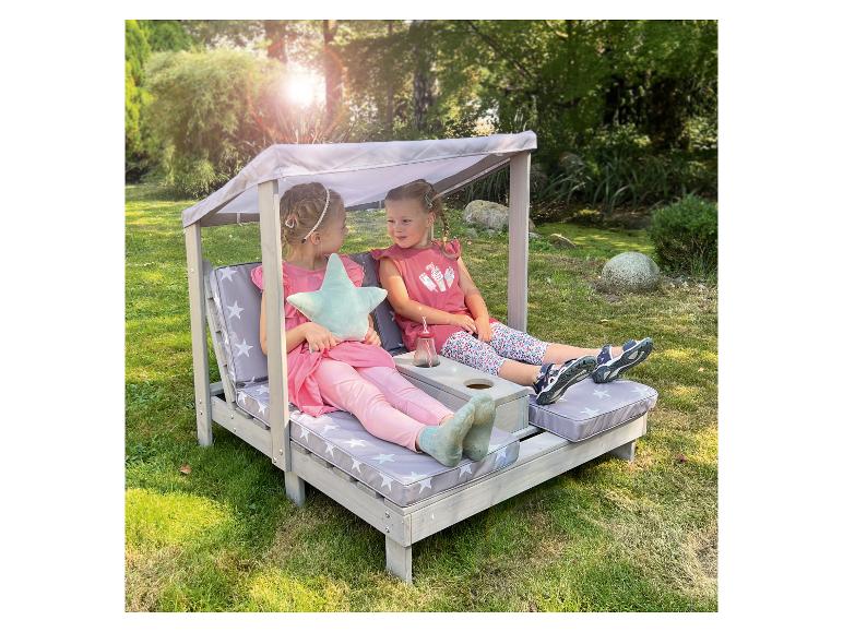 Zwei kleine Mädchen entspannen auf einer hölzernen Gartenliege mit Sternenkissen.