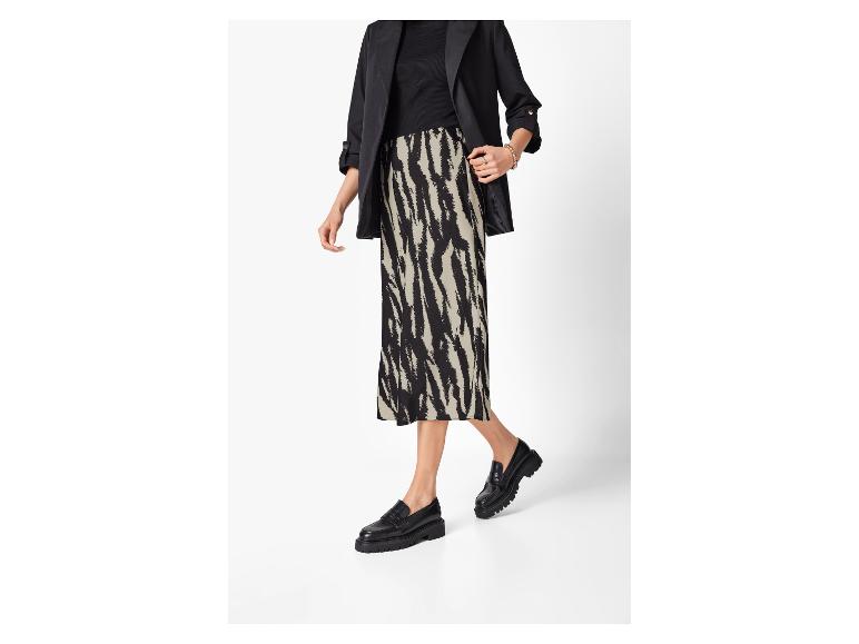 Frau in schwarzem Blazer, schwarzem Oberteil, gemustertem Rock und schwarzen Loafern.